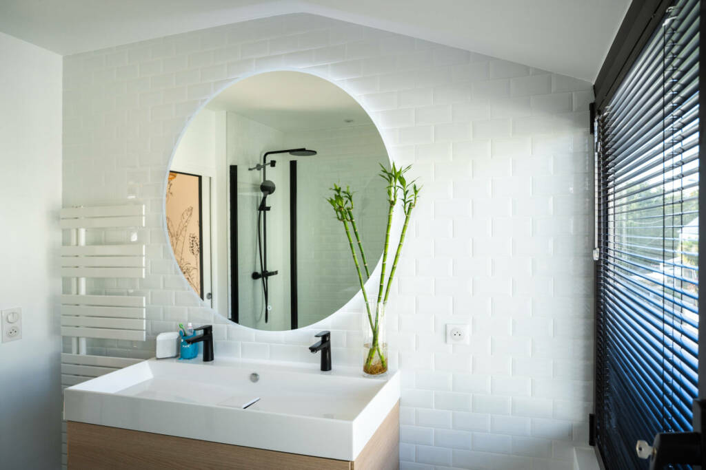 Une grande vasque rectangulaire et un miroir rond comme un soleil sur un carrelage blanc façon métro, par l'Agence Bérénice Alandi, Architecte d'intérieur en Finistère Sud 29