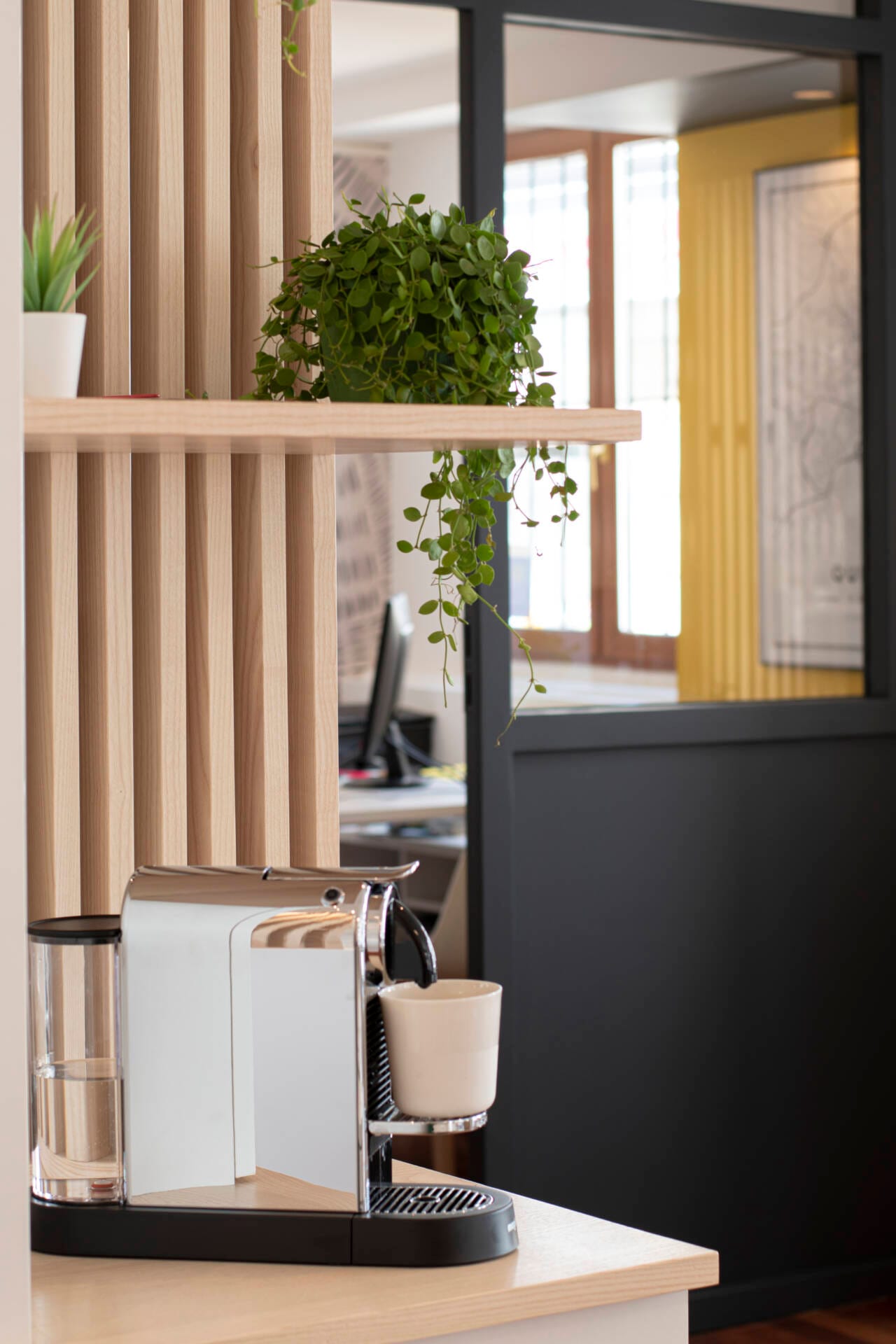 Vue de l'agencement avec claustras et de la verrière noire du bureau de l'agence immobilière par l'Agence Bérénice Alandi, Architecte d'intérieur en Finistère Sud 29